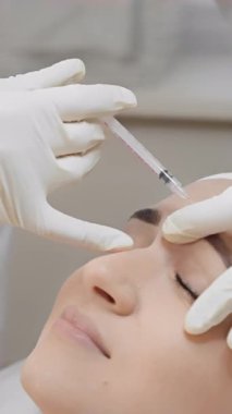 Görüntü, estetik bir prosedürde kırışıklıkları azaltmak ve genel güzelliği arttırmak için hastanın kaşlarının yakınına botulinyum enjekte eden yetenekli bir tıp uzmanını gösteriyor.