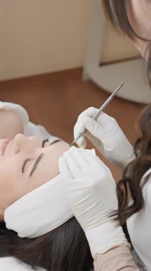 Deneyimli bir kozmetolog, sakin bir klinikte gelişmiş cilt bakımı teknikleri kullanarak tatmin olmuş bir hastaya hassas bir yüz tedavisi uygular.