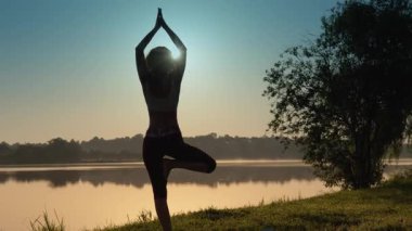 Gün doğumunda yoga yapan bir kadın silueti sakin bir göl kenarında vücut ve zihni uyumlu hale getiriyor. Şafağın doğuşu huzurlu atmosferi güçlendirir, ortama sakinlik katar.