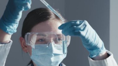 Laboratuvarda, koruyucu giyimli bir bilim adamı, etkili aşılar geliştirmek ve hastalıklara karşı tedavileri geliştirmek için hayati önem taşıyan bir araştırma yürüterek, bir test tüpünü dikkatle kullanır.