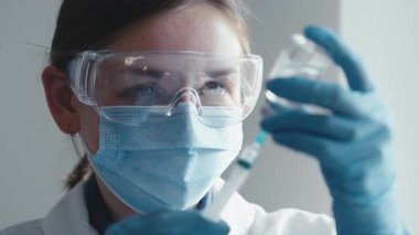 Laboratuvar önlüklü kendini adamış bir bilim adamı titizlikle şırınga ve şişeyle bir aşı hazırlıyor. İlaç araştırma ve geliştirmede olağanüstü hassasiyet gösteriyor.