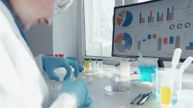 Laboratuvar önlüğü ve eldivenleriyle kendini adamış bir bilim adamı bilgisayar ekranındaki verileri incelerken aşı geliştirme konusundaki bilimsel araştırma sürecini gözler önüne seriyor..