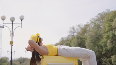 Sıcak ve güneşli bir günde, genç bir kadın canlı sarı bir bavulun üzerinde uzanırken neşe bulur. Yaz tatillerinin özünü yakalıyor ve ruhunu tanımlayan tasasız yolculukları kucaklıyor.