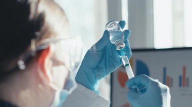 Yoğun bir laboratuvarda, beyaz önlüklü bir bilim adamı bilimsel araştırmaların titiz doğasını modern bir laboratuvar ortamında gösteren bir şırınga ve şişeyle aşıyı dikkatlice hazırlıyor.