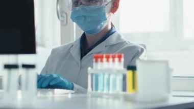 Koruyucu ekipman kullanan kendini adamış bir bilim adamı, steril bir ortamda analiz için aşı örnekleri hazırlıyor ve modern araştırmaların halk sağlığı ve güvenliğini artırmadaki önemini vurguluyor.