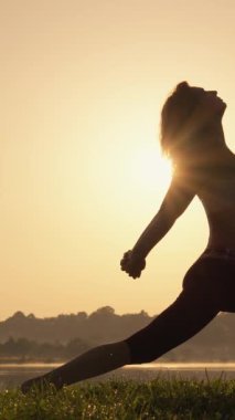 Gün batımında yoga yapan güzel ve dingin bir kadın silueti. Sıcak güneş sakin bir ufkun ardında yavaşça batarken iç huzur ve denge duygusunu somutlaştırıyor.