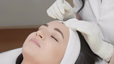 Uzman bir kozmetik uzmanı bir müşteriye cilt bakımı yapar, gelişmiş teknikler gösterir ve profesyonel bir klinikte rahatlatıcı bir ortam sağlar. Cilt tazeleme vurgusu.