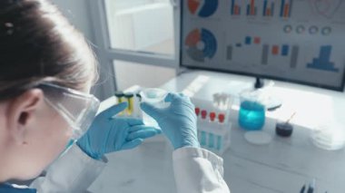 Laboratuvar önlüğü giymiş odaklanmış bir bilim adamı, bir ekrandaki renkli test tüpleri ve istatistiksel verilerle çevrili petri kabındaki bir örneği inceleyerek aşı gelişimini ve bilimsel araştırmaları resmediyor..