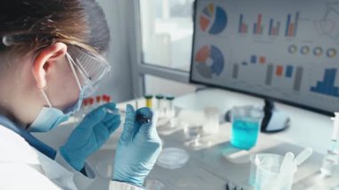 Odaklanmış bir bilim adamı laboratuvarda çalışıyor, örnekleri inceliyor ve bir monitördeki verileri analiz ediyor, tıp ve aşı geliştirme çalışmalarının önemini vurguluyor.