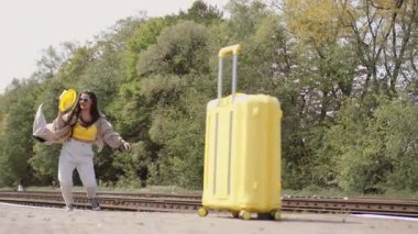 Hayat dolu genç bir kadın, sarı bavulunun yanında heyecanla sıçrıyor. Keşfedilmeyi bekleyen sonsuz bir keşif ve eğlenceyle dolu bir yaz yolculuğuna çıkmanın heyecanını simgeliyor.