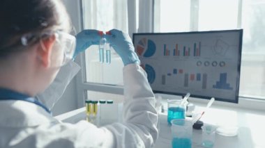 Laboratuvar önlüğü giymiş kendini adamış bir bilim adamı parlak bir pencerenin kenarında biyolojik örnekler üzerinde karmaşık deneyler yapıyor ve yakınlardaki bir bilgisayar ekranında gösterilen sonuçları titizlikle analiz ediyor.