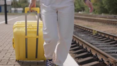 Genç bir kadın, hareketli bir tren peronunda güvenli adımlarla yürüyor, parlak sarı bir bavul çekiyor, yaz yolculuğunun maceraperest ruhunu somutlaştırıyor ve önlerindeki keşiflerin sevincini.