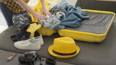Hevesli bir insan sevinçle renkli kıyafetler ve aksesuarlarla dolu parlak sarı bir bavul topluyor. Keşif ve yeni deneyimlerle dolu heyecanlı bir seyahat macerası için.