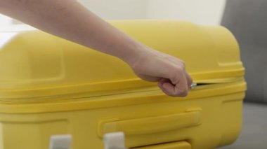 Yakından çekilen bir fotoğraf güzel bir el yakalıyor canlı ve göz alıcı sarı bir valizin fermuarını açıyor, önümüzde heyecanlı bir tatil için hazırlanmanın heyecanlı başlangıcını işaret ediyor.