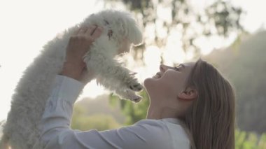 Güzel bir açık hava ortamında, bir kadın tüylü köpeğini neşeyle havaya kaldırır, sevgi, arkadaşlık ve evcil hayvan sahibi olmanın saf sevinci ile dolu, doyurucu bir anda eğlenir.