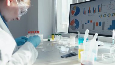 Beyaz önlüklü kendini adamış bir bilim adamı yüksek teknoloji ekranında örnekler ve karmaşık verileri analiz ediyor, özellikle de yenilikçi aşı geliştirme alanındaki gelişmeleri vurguluyor.