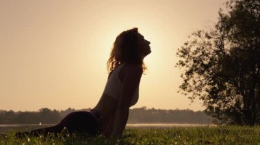 Bir birey şafak vakti göl kenarında yoga yapar, güneşin getirdiği huzur ve uyumu vurgular, özenli ve sakin bir atmosfer yaratır güzellik