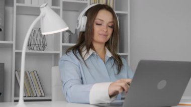 Modern bir ev ofisinde, açık mavi gömlekli genç bir kadın, bu dingin alanda üretkenliğini yansıtan, neşeli müzikler dinlerken, işine dalmış bir şekilde dizüstü bilgisayarına odaklanıyor.