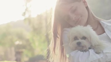 Güneşli bir açık hava ortamında, genç bir kadın tüylü köpeğini beşiğinde, sıcaklığını ve arkadaşlığını paylaşırken bu huzur ve neşe dolu anda doğanın canlı güzelliğinin tadını çıkarıyor.