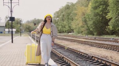 Yoğun bir tren istasyonunda, genç bir kadın parlak sarı bavuluyla güven içinde duruyor, sonsuz olanaklarla dolu heyecanlı yaz tatiline hazırlanıyor.