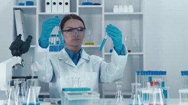 Odaklanmış bir bilim adamı yüksek teknolojili bir laboratuvarda farklı test tüplerini inceler. Olay yeri, bilimsel araştırmaların önemini vurgulayarak titiz bir araştırma ve analiz gösteriyor..