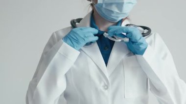 Beyaz önlüklü ve steril eldivenli kendini adamış bir sağlık uzmanı steteskopunu ayarlıyor ve klinik bir ortamda mükemmel bir bakım sağlamaya hazır olduğunu gösteriyor.