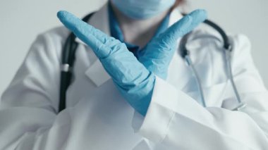Tıbbi bir ortamda, laboratuvar önlüğü ve eldiven giyen bir profesyonel, sürmekte olan salgın sırasında sağlık bilincinin ve önleyici tedbirlerin önemini vurgulamak için el hareketlerini kullanır.
