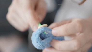 Parmaklar, tekstil sanatı ve tasarım alanındaki yaratıcılığı ve dokunsal bağlılığı ortaya koyan gelişmiş teknikler sergileyerek, yumuşak mavi ipliği ustalıkla idare ediyor.