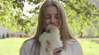 Bu yürek ısıtan sahne, genç bir kızın sevgili küçük köpeğiyle nazikçe etkileşime geçişini sergiliyor. Açık havada huzurlu bir ortamda, aralarında paylaşılan değerli sevgi anlarını yakalıyor.