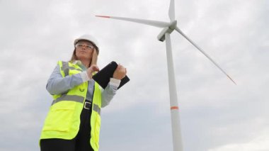 Güvenlik teçhizatında yetenekli bir kadın mühendis tabletiyle rüzgar türbinlerini değerlendiriyor, yenilenebilir enerjinin yönetiminde hayati rol oynuyor ve sürdürülebilir bir gelecek için mühendislik yapıyor.