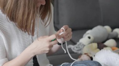 Odaklanmış bir kadın, rahat ve davetkar bir ortamda el işçiliğinin zevkini yansıtan renkli ipliklerle çevrelenmiş bir şekilde büyüleyici bir pelüş oyuncağı ustalıkla örüyor.