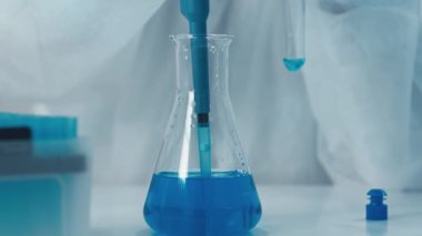 Yetenekli bir laboratuar teknisyeni, kalibre edilmiş bir pipetten, önemli bilimsel araştırmaları yürütürken hassas olduğunu gösteren bir test tüpüne canlı mavi bir sıvı aktarıyor.