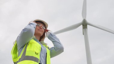 Güvenlik teçhizatı alanında yetenekli bir kadın mühendis, sürdürülebilir enerjide parlak bir geleceği sembolize eden ve yenilenebilir kaynak yeniliğindeki hayati rolünü vurgulayan büyük bir rüzgar türbini araştırıyor.