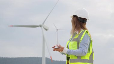 Güvenlik teçhizatı alanında çalışan bir kadın mühendis, yenilenebilir enerji konusunda yenilikçi bir düşünce sergileyen minyatür bir rüzgar türbini modeli üzerinde çalışıyor. Sahne sürdürülebilirliği ve modern mühendisliği vurguluyor.