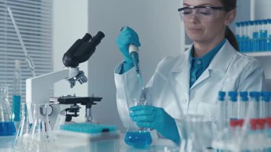 Bilimsel aletlerle donatılmış modern bir laboratuvarda, çok yetenekli bir laboratuvar teknisyeni titizlikle bilim alanında kesin deneyler yapmak için bir mikro pipet kullanıyor.