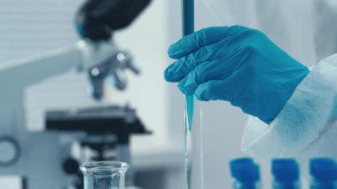 Yetenekli bir teknisyen deney tüpleri ve mataralar arasında canlı mavi sıvıyı aktarmak için pipet kullanır. Kimyasal analiz ve deney tekniklerinde hassasiyet gösterir.