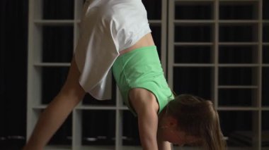 Yoga yapan bir kız, yere bakan bir köpek. Onun yeşil bir gömleği ve beyaz bir eteği var. Beyaz rafları ve karanlık arka planı olan bir odada. Formuna ve sağlığına odaklan..