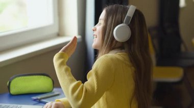 Genç bir kız pencerenin yanındaki mavi bir masada oturuyor, kulaklık ve sarı bir kazak giyiyor. O, bir jest olarak elini kaldırarak müziğe eşlik eder. Kalem kutusu ve defter masanın üstünde..