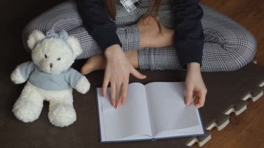 Yanında pelüş bir oyuncak ayı olan biri açık bir defterle yan yana oturur. Sahne yumuşak bir paspasın üzerine kurulmuş, rahatlatıcı bir öğrenme atmosferi yaratıyor..