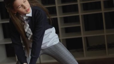 Bir kız donanma üniforması, pantolon ve kravat takıyor. O muhtemelen bir dans pratiği yapıyor. O, gözleri kapalı öne doğru eğiliyor. Uzun saçları var ve küçük bir küpe takıyor.. 