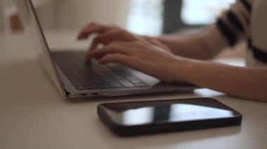 Görüntü, günümüzde dijital bağlantının önemini ve modern çalışma alanını vurgulayan akıllı bir telefonla dizüstü bilgisayarda yazı yazan ellerin yakın çekimini gösteriyor.