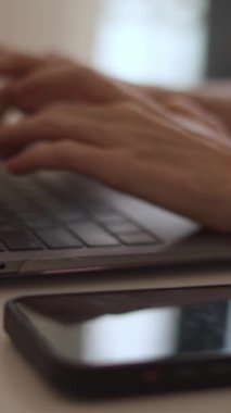 Görüntü, günümüzde dijital bağlantının önemini ve modern çalışma alanını vurgulayan akıllı bir telefonla dizüstü bilgisayarda yazı yazan ellerin yakın çekimini gösteriyor.
