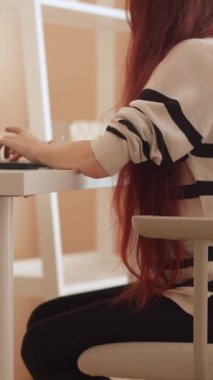 Uzun saçlı yetenekli bir kadın, yaratıcı görevleri için üretkenliği ve modern yaşamı somutlaştıran ılık ışık ve yumuşak pastellerle dolu minimalist bir çalışma alanında, parlak dizüstü bilgisayarıyla çalışır.