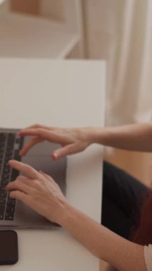 Uzun kızıl saçlı genç bir kadın, üretkenliği yaratıcı ifade ve ilhamla harmanlayan modern uzak çalışma yaşam tarzını benimsemek için özenle dizüstü bilgisayarında çalışıyor.