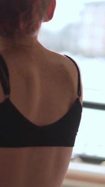 Sıcak yatak odasında, genç bir kadın güne hazırlanmak için acele etmez. Sabahki titreşimlerin sakinliğini hisseder ve pencereye dökülen sıcak ışığın altında kıyafetlerini ayarlar.