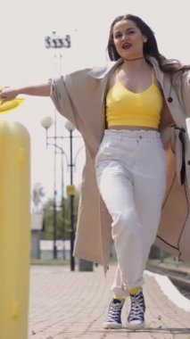 Renkli yaz kıyafetleri içinde hayat dolu genç bir kadın hareketli bir tren istasyonunda bir bavulla neşeli bir şekilde geziniyor, heyecanlı ve manzaralı bir yolculuk için hazır hissediyor.