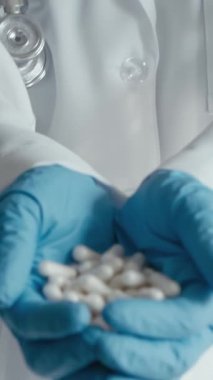 Beyaz önlüklü ve mavi eldivenli bir sağlık uzmanı çeşitli beyaz kapsüller sunarak, etkili tıbbi tedavi ve hasta bakımında ilaçların hayati rolünü vurguladı.