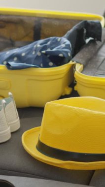 Parlak sarı bir bavul, içi seyahat gereksinimleriyle dolu iyi korunmuş bir iç mekan gösteriyor. Yakınlarda, taze beyaz ayakkabılar, parlak sarı bir şapka ve önümüzde heyecan verici maceraları bekleyen bir kamera.