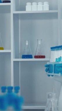 Çağdaş bir laboratuvar ortamında, gerekli koruyucu malzemelerle süslenmiş çalışkan bir laboratuvar bilimcisi, önemli araştırma girişimlerini temsil eden çeşitli test tüplerini titizlikle inceliyor.