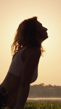 Bir birey şafak vakti göl kenarında yoga yapar, güneşin getirdiği huzur ve uyumu vurgular, özenli ve sakin bir atmosfer yaratır güzellik